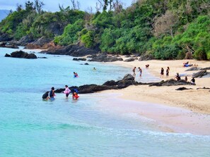 A beach with clear turquoise water, rocky shoreline, and people engaging in water activities. - Nirai Onna (Onna)