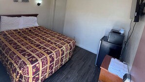 A hotel room with a bed, a desk, a trash bin, a wall-mounted TV, and a ceiling light fixture. - World Motel (Lynwood)
