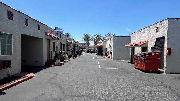 A street with buildings, a clear sky, and a red dumpster. - World Motel (Lynwood)