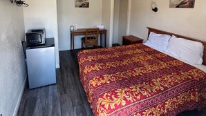A bedroom with a bed, a desk, a chair, a small refrigerator, and a television on the wall. - World Motel (Lynwood)