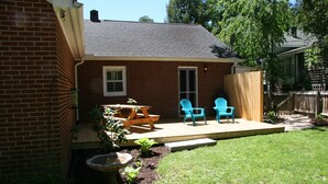 A backyard with a brick house, a wooden deck, two blue chairs, a table, and a potted plant. - GASLIGHT COTTAGE  - Downtown Hendersonville (Hendersonville)