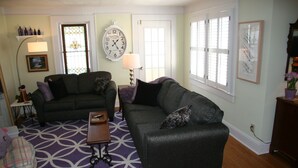 A living room with two dark grey sofas, a patterned rug, a wall clock, and a window with blinds. - GASLIGHT COTTAGE  - Downtown Hendersonville (Hendersonville)