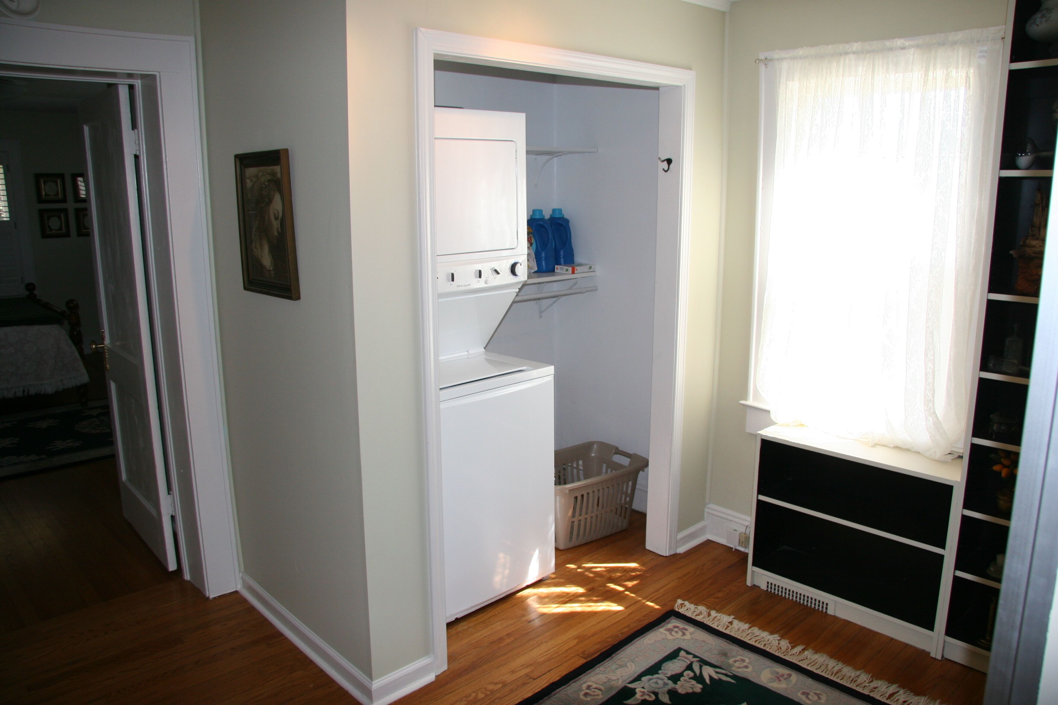 A laundry room with a washing machine, a drying rack, and a window with curtains.