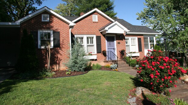 A two-story brick house with a front porch, a small garden, and a red flowering bush. - GASLIGHT COTTAGE  - Downtown Hendersonville (Hendersonville)