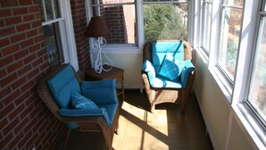 A sunlit room with wicker chairs and a table, large windows, and a brick wall. - GASLIGHT COTTAGE  - Downtown Hendersonville (Hendersonville)