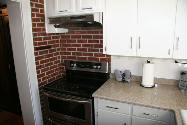 A kitchen with a brick backsplash, stainless steel appliances, white cabinets, and a granite countertop.