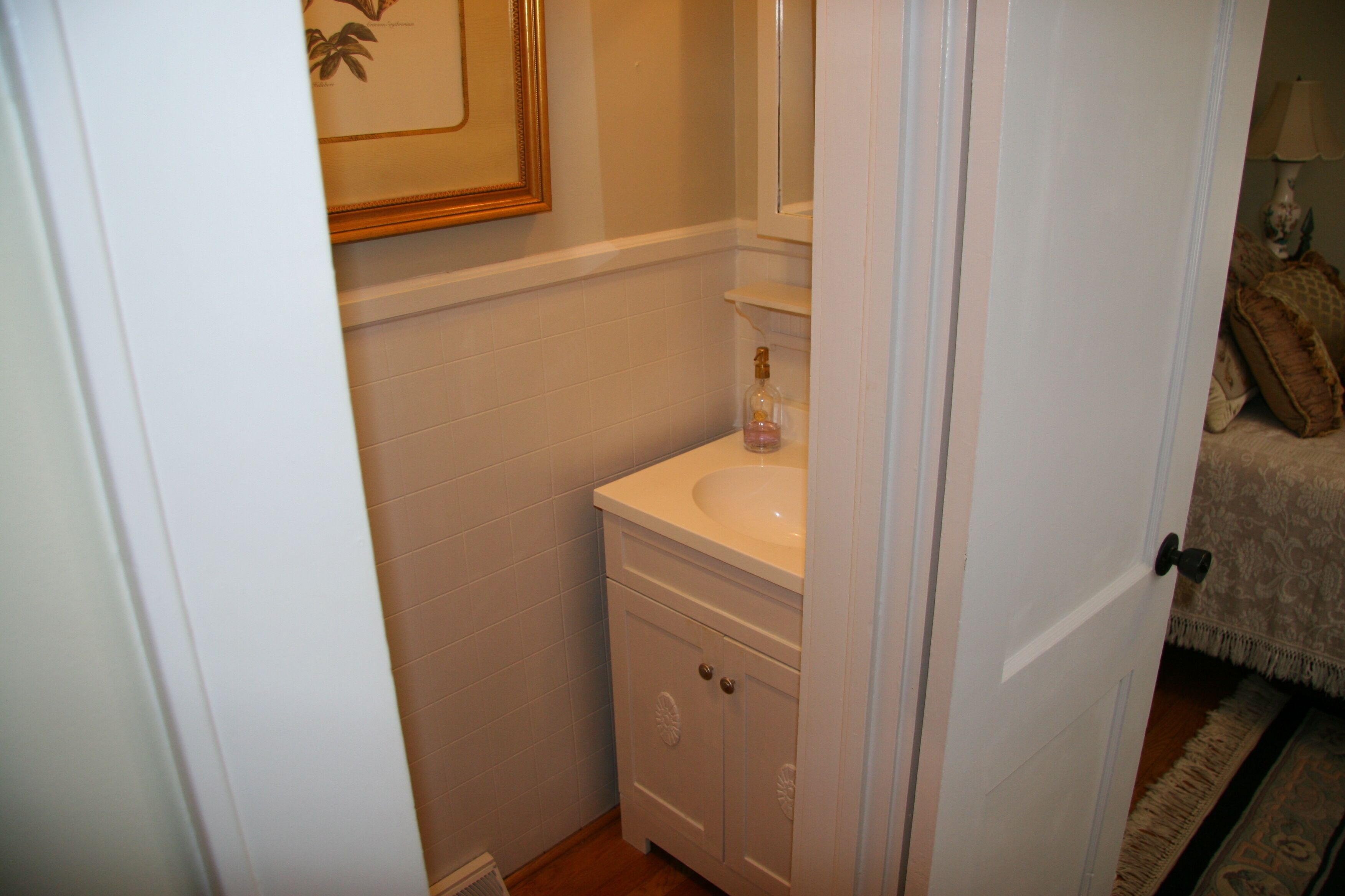 A bathroom with a white sink, a mirror above it, and a framed picture on the wall.
