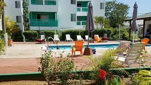 A pool area with lounge chairs and umbrellas, surrounded by greenery and a building with green balconies. - Cozy Condo on the Beach (Negril)