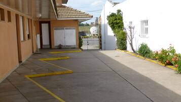 A narrow street with yellow lines, a building with a tiled roof, and a white building with a fence and plants.