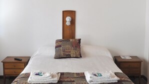 A neatly made bed with a wooden headboard, two bedside tables, and a quilted bedspread. - Hotel Venezia (Necochea)