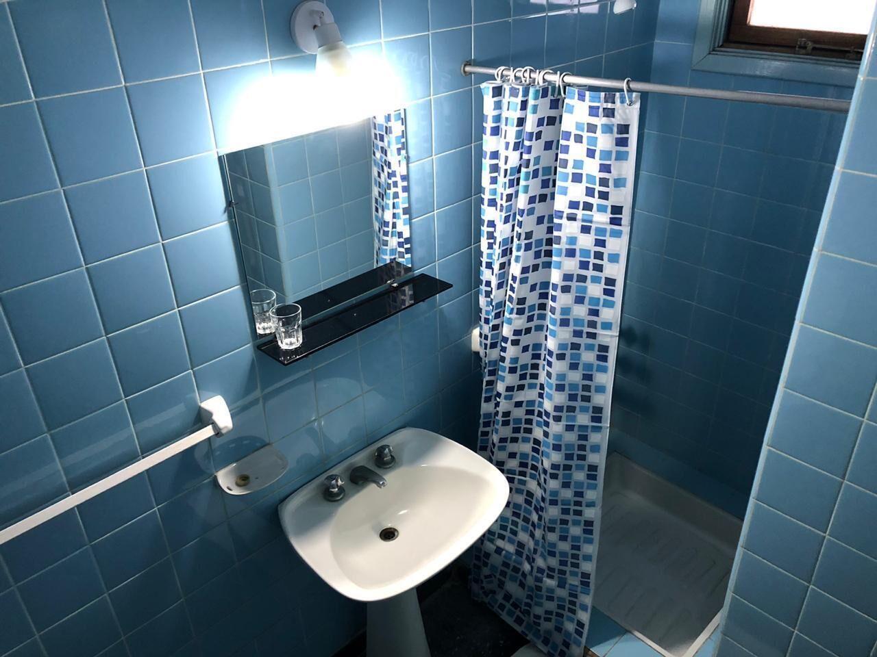 A bathroom with blue tiles, a white sink, a glass shelf, and a shower curtain.
