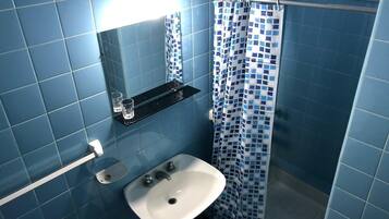A bathroom with blue tiles, a white sink, a glass shelf, and a shower curtain.
