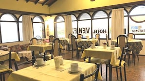A hotel dining area with multiple tables set for breakfast, featuring yellow tablecloths and chairs. - Hotel Venezia (Necochea)