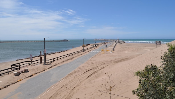 A beach with a paved walkway, a fence, and a pier in the distance. - Hotel Venezia (Necochea)