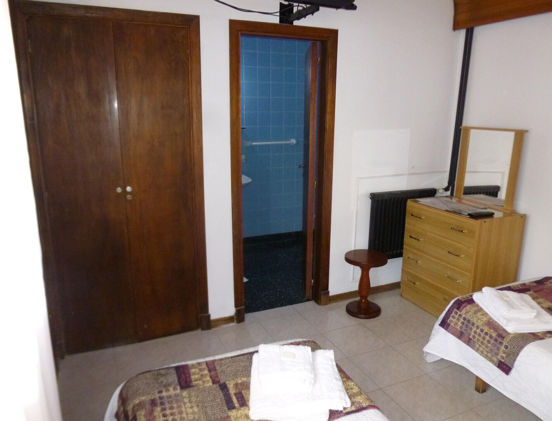 Een slaapkamer met een houten garderobe, een badkamer met blauwe tegels, een houten dressoir en een bed met een bedsprei met dessin.