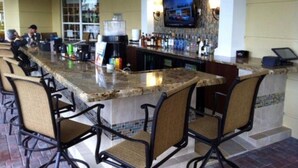 Un espace bar doté d’un long comptoir, de tabourets de bar, d’un téléviseur fixé au mur et d’une enseigne au-dessus du comptoir.