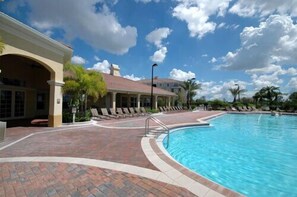Uma área de piscina com piscina azul cristalina, um alpendre coberto com espreguiçadeiras e um edifício com telhado em azulejos.