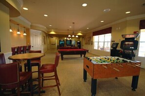 Uma sala de jogos com mesa de bilhar, mesa de futebol de mesa e um bar com cadeiras e mesa.