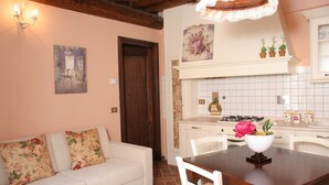 A cozy living room with a sofa, a dining table with chairs, a kitchen area with a stove, and a decorative wall piece.