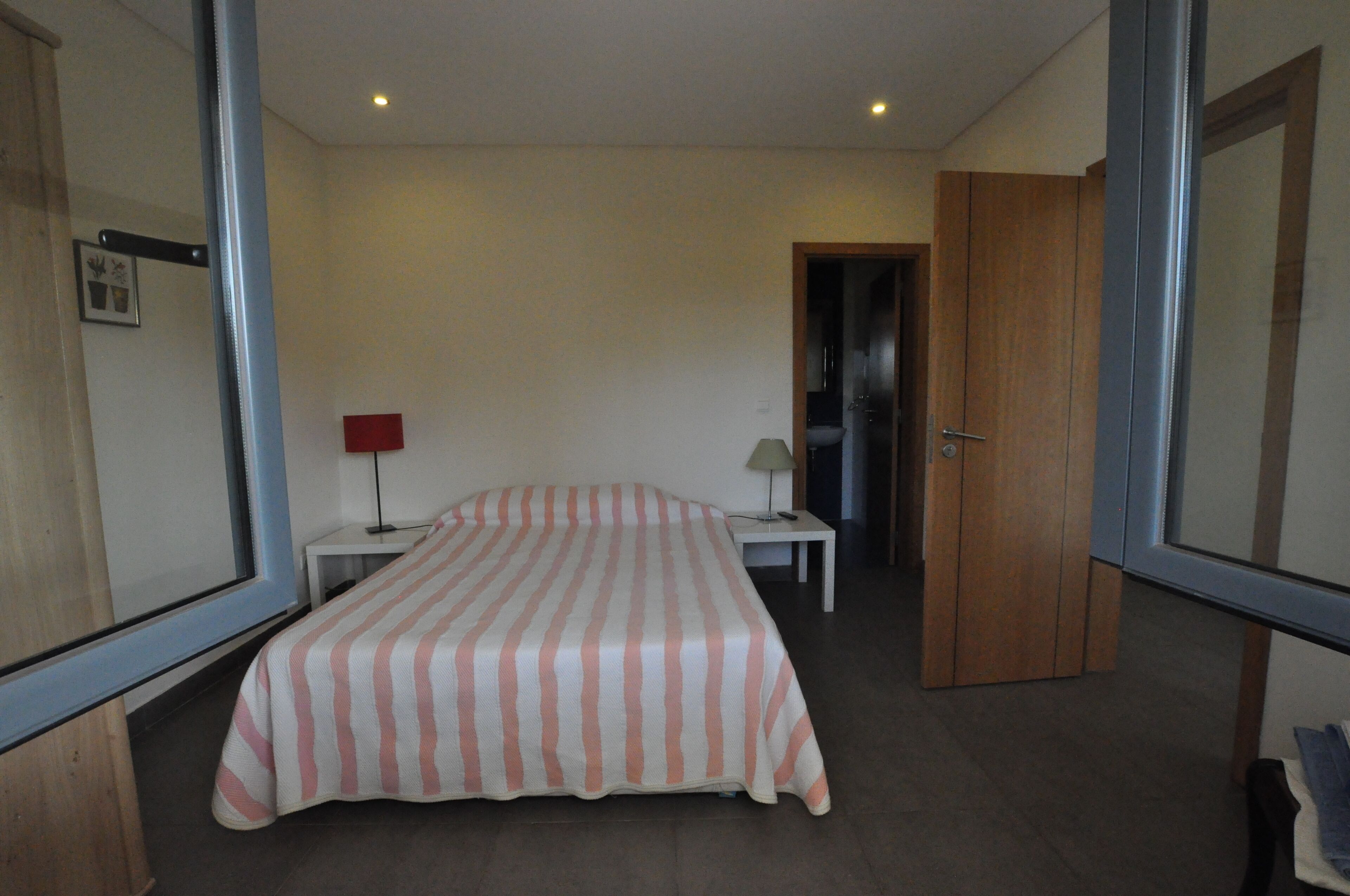 Une chambre à coucher comprenant un lit, deux tables de chevet, une commode, une porte et un miroir.