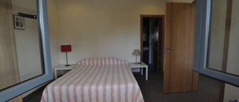 Une chambre à coucher comprenant un lit, deux tables de chevet, une commode, une porte et un miroir.