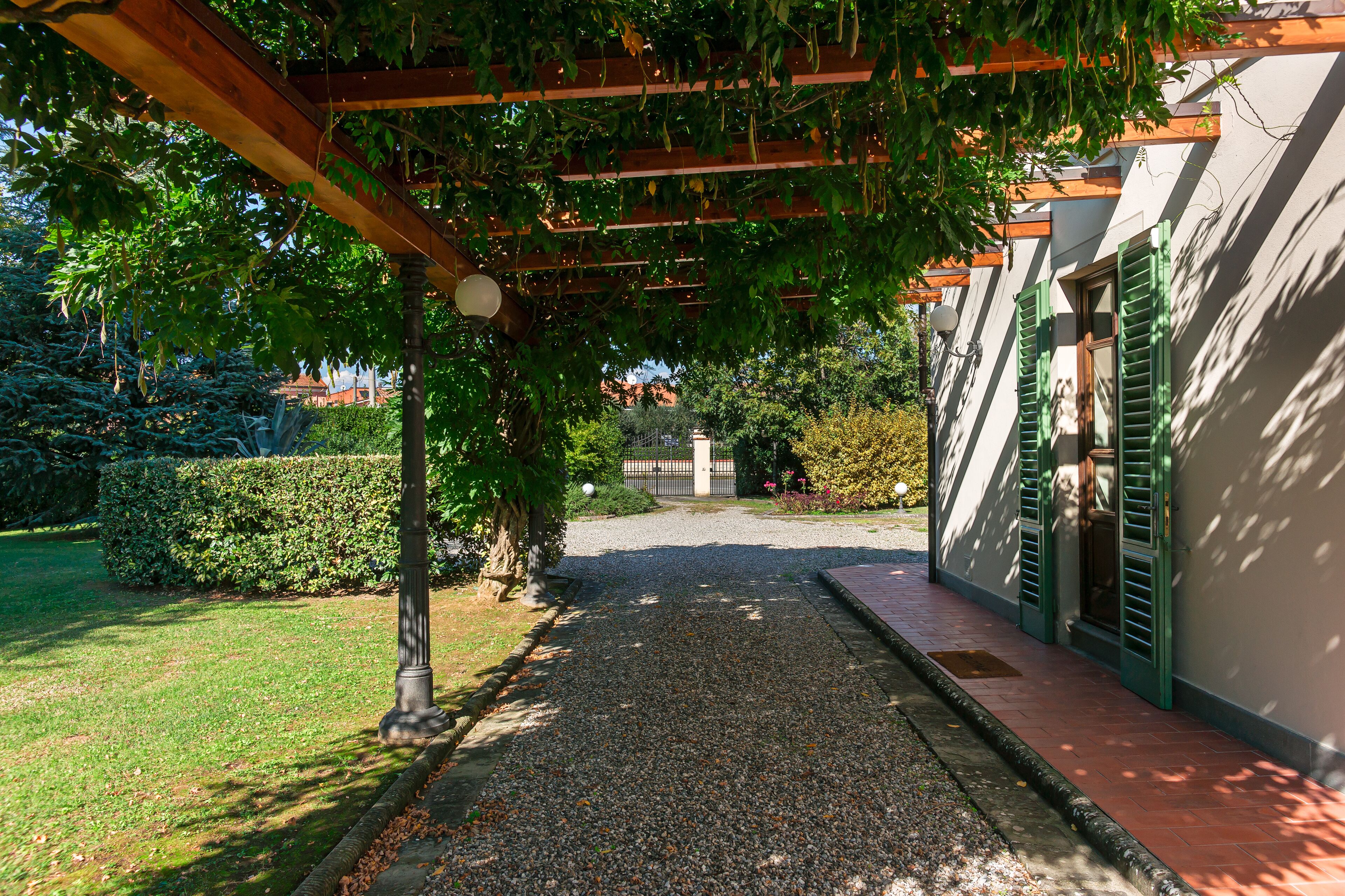 A gravel pathway leading to a building with a pergola overhead.