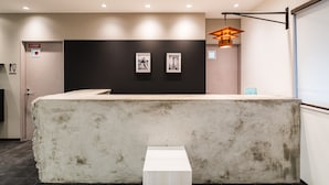 A reception area with a reception desk, two framed pictures on the wall, a small table, and a door with a sign. - OKINI - DOYANEN HOTELS (Osaka)