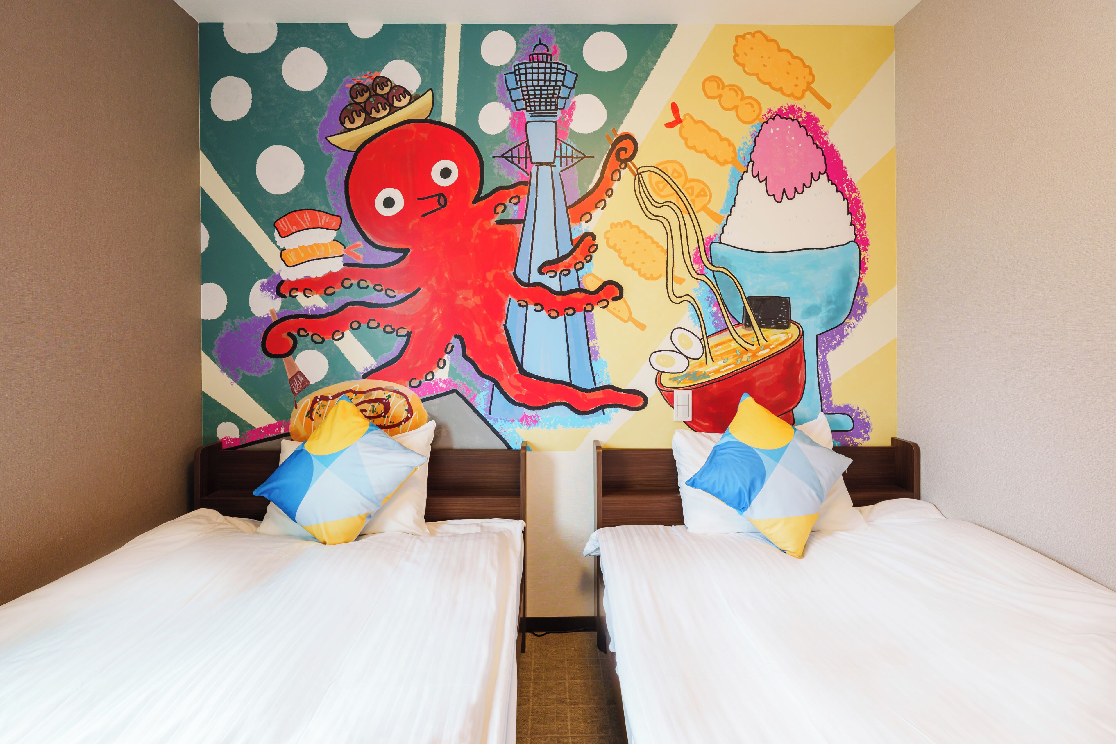 Ett hotellrum med två sängar, en färgstark väggmålning och utsikt över staden.