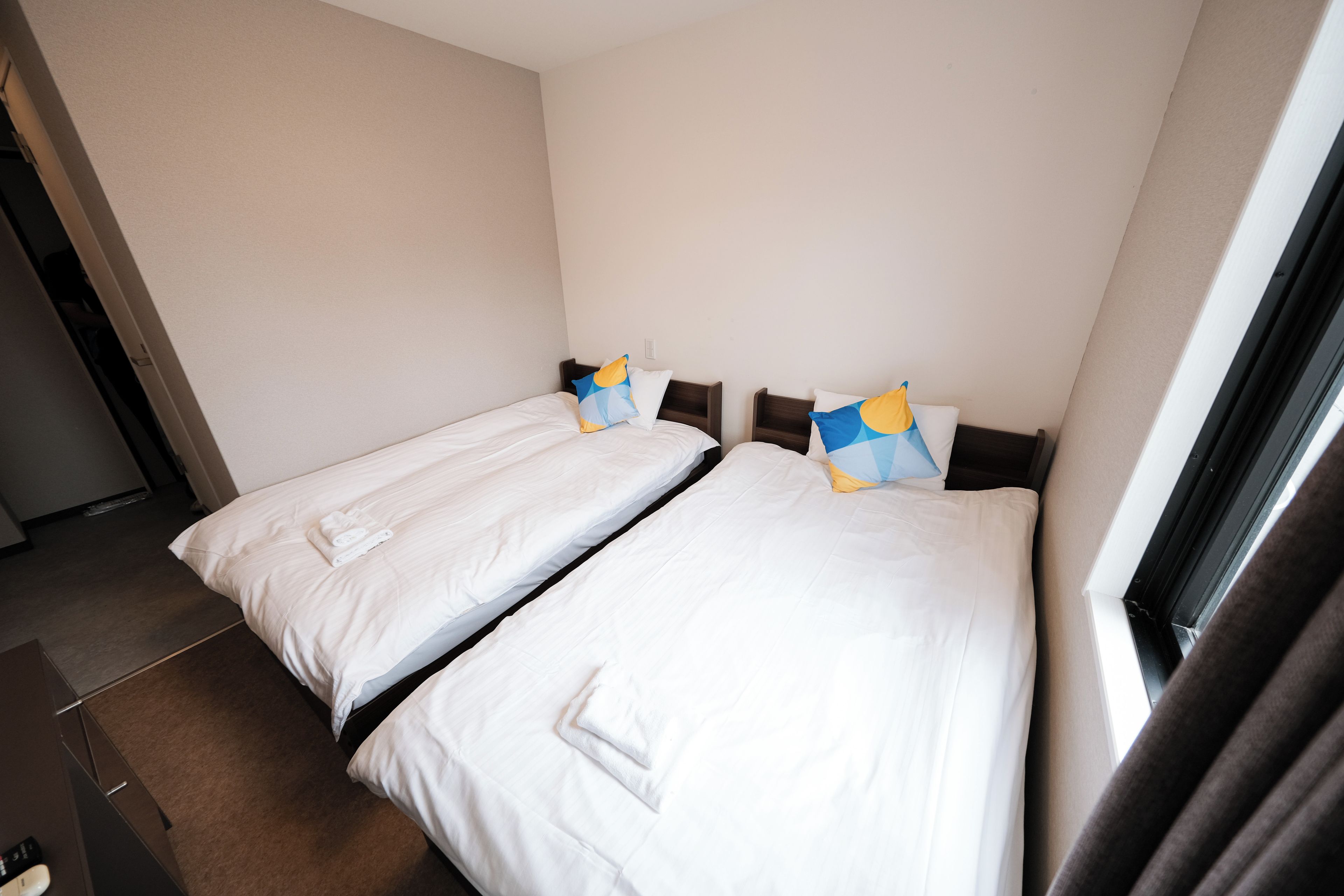 Ein Hotelzimmer mit zwei Einzelbetten, jeweils mit einem Kissen und einem ordentlich gefalteten Handtuch.
