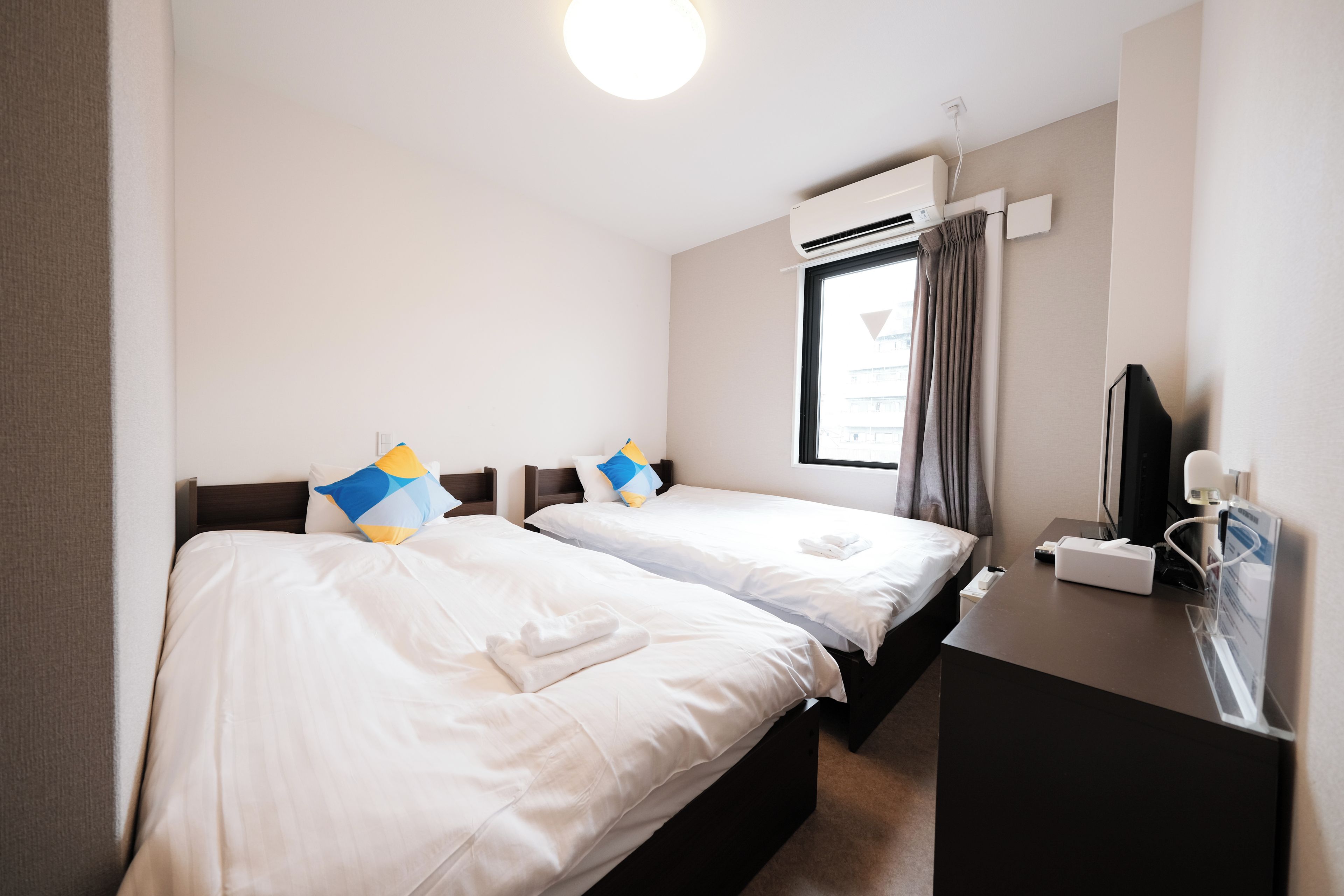 A hotel room with two beds, a desk, a mirror, and an air conditioning unit.