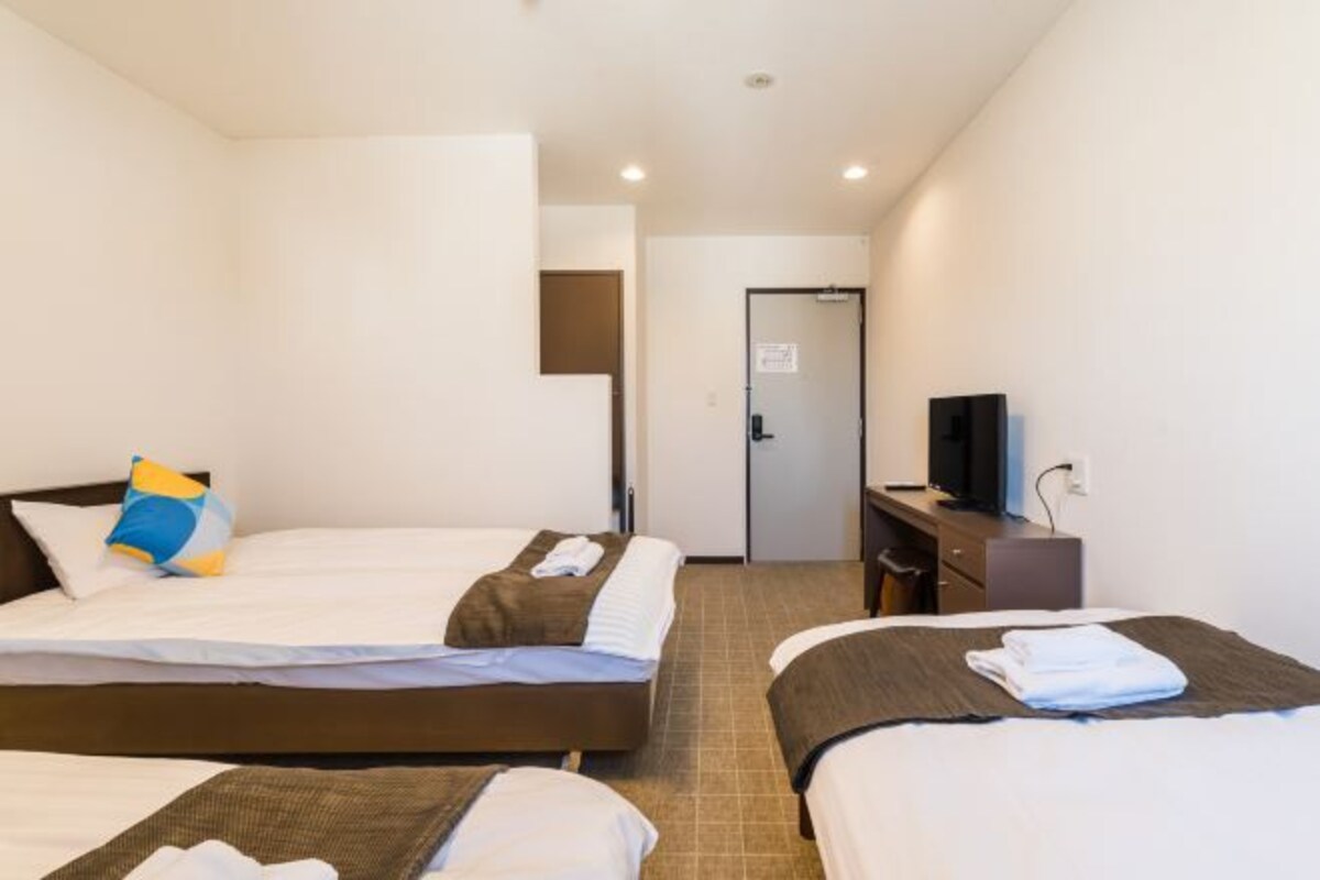 A hotel room with two beds, a desk with a computer, a TV, and a door leading to a bathroom.