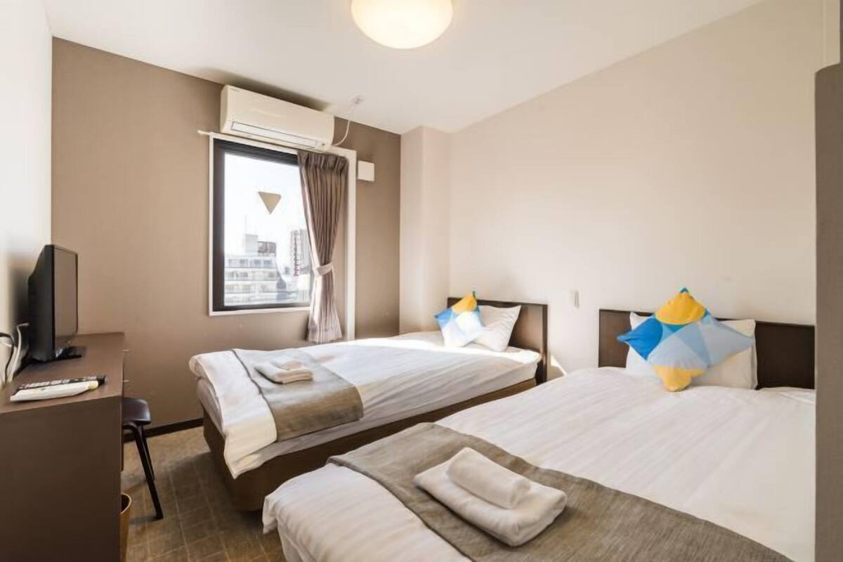 A hotel room with two beds, a desk with a computer, and a window with curtains.