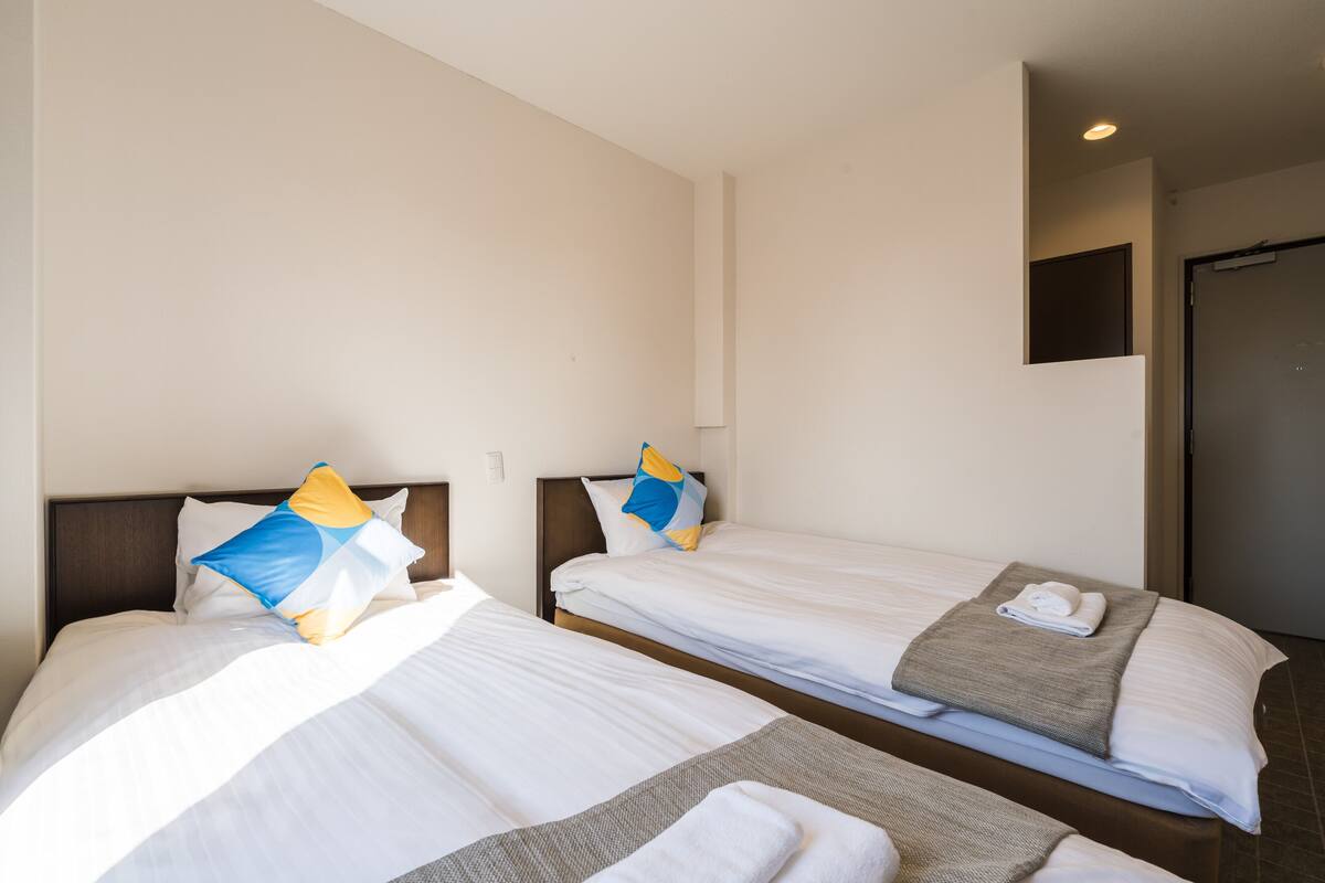 A hotel room with two single beds, each with a pillow and a blanket.