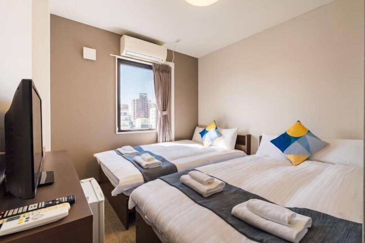 A hotel room with two beds, a desk with a computer, a TV, and an air conditioning unit.