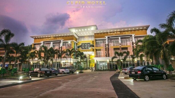The exterior of Cupid Hotel Trang with multiple floors, palm trees, and a parking area. - Cupid Hotel (Palian)