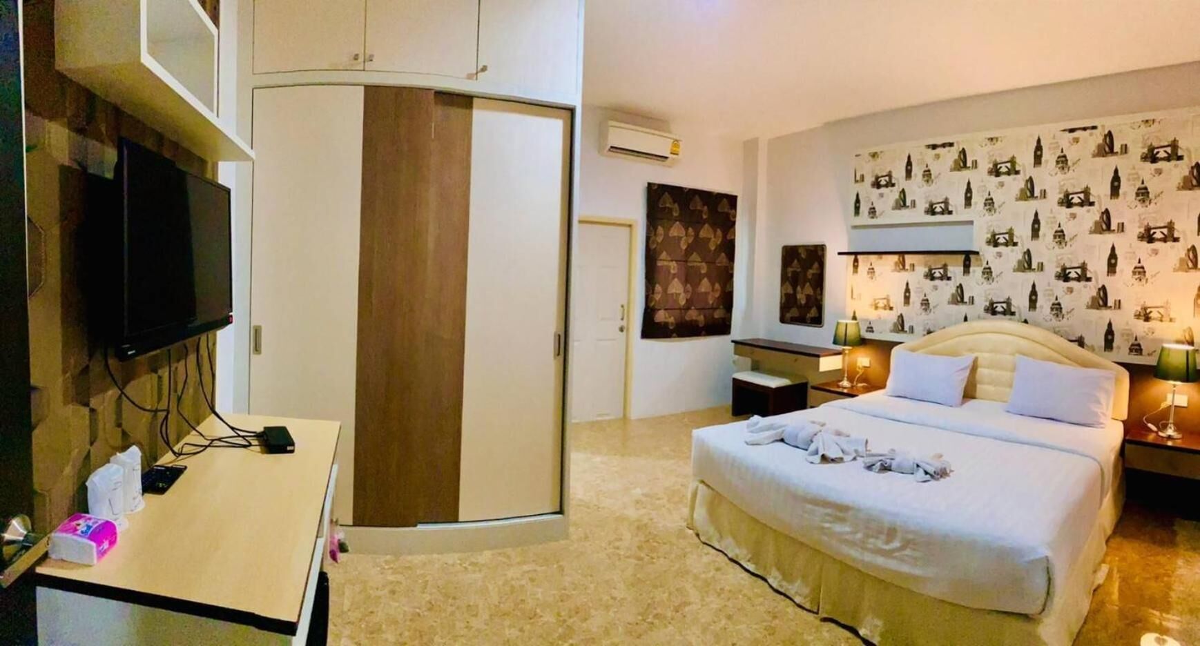 A hotel room with a bed, bedside tables, a desk, a TV, and a wardrobe.