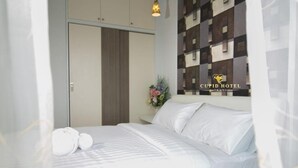 A hotel room with a bed, a nightstand with a vase of flowers, and a wall with a checkered pattern. - Cupid Hotel (Palian)