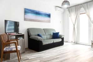 A living room with a grey sofa, a wooden chair, a flat-screen TV, and a painting of a beach scene.