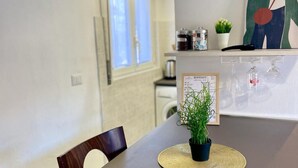 Une cuisine moderne avec un coin repas. On y trouve un tableau affichant le menu, une plante en pot et une fenêtre avec des stores.
