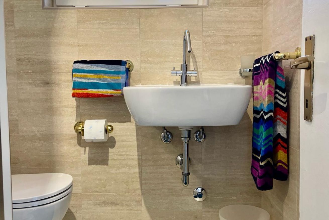 Une salle de bain avec un lavabo blanc, des toilettes et un porte-serviettes orné de serviettes colorées.