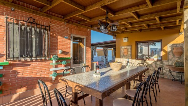 An outdoor patio with a wooden table and chairs, a brick wall, and a stone wall with windows. -  House Ludima in Fuentes de Andalucia, 40 min from Sevilla and 50 min of Cordoba (Fuentes de Andalucía)