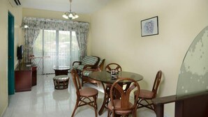 A dining area with a round table and chairs, a small round table, a sofa, and a TV. - May Condo (Langkawi)