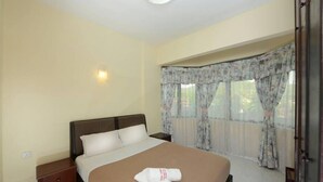 A hotel room with a bed, a nightstand, a window with curtains, and a wall-mounted light. - May Condo (Langkawi)