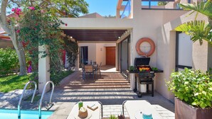 Un área de piscina con un pérgola, mobiliario exterior y una parrilla.