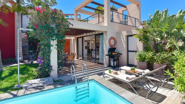 Una casa moderna con piscina, mobiliario exterior y zona de barbacoa.
