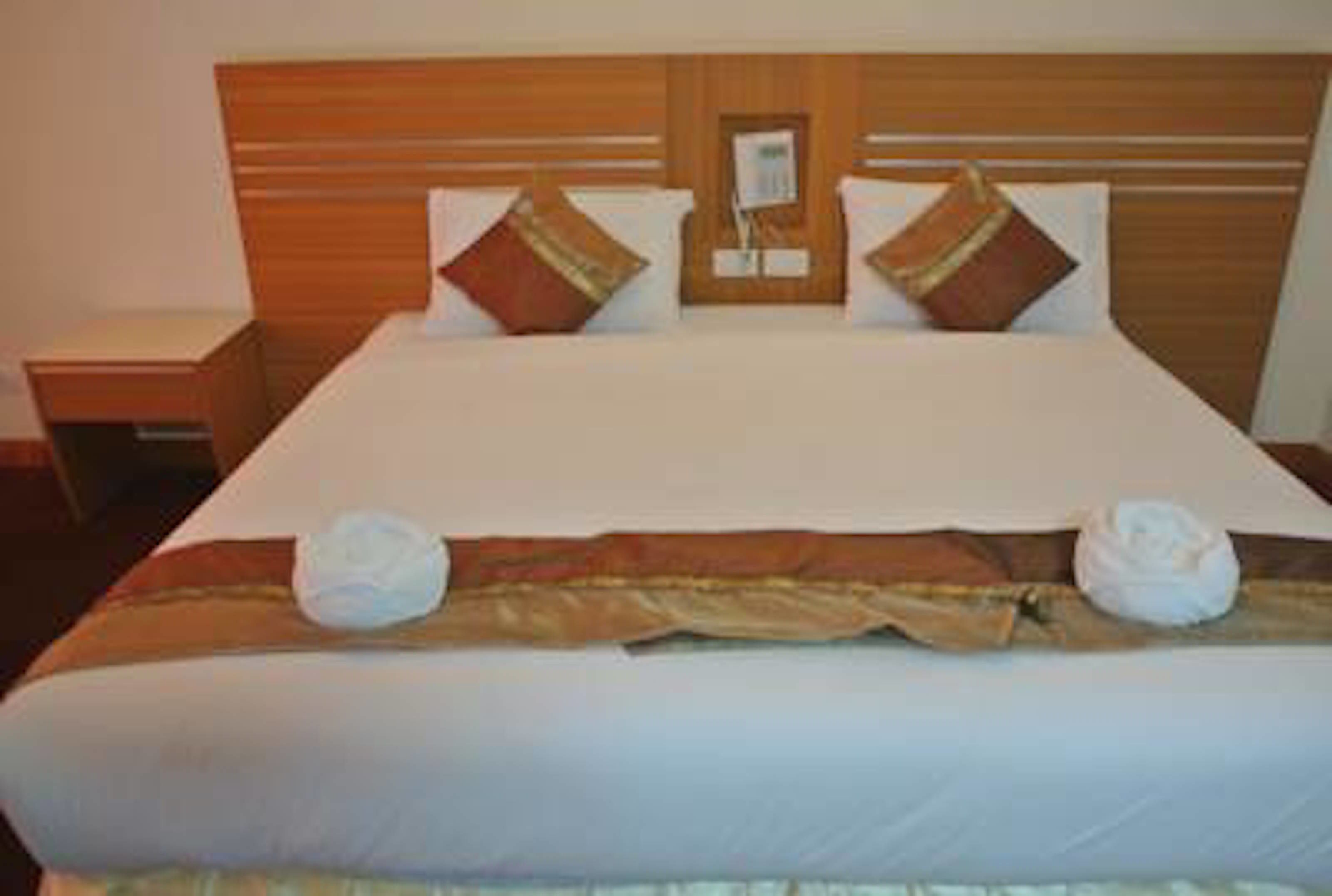 Una habitación de hotel con una cama grande, cabecero de madera, dos mesitas de noche y un tocador.