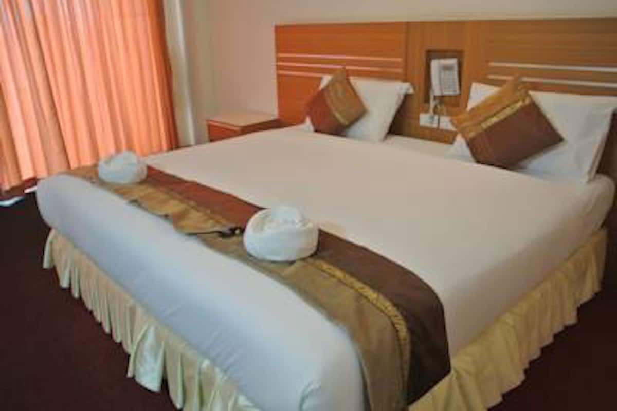 A hotel room with a large bed, a wooden headboard, a nightstand, and a window with curtains.