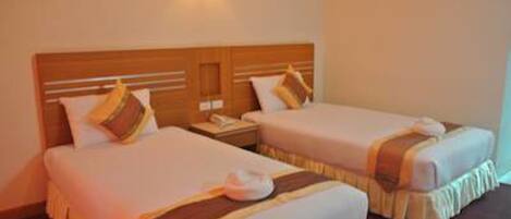 Habitación de hotel con dos camas, cada una con cabecero de madera, ropa de cama blanca y una mesita de noche con lámpara.