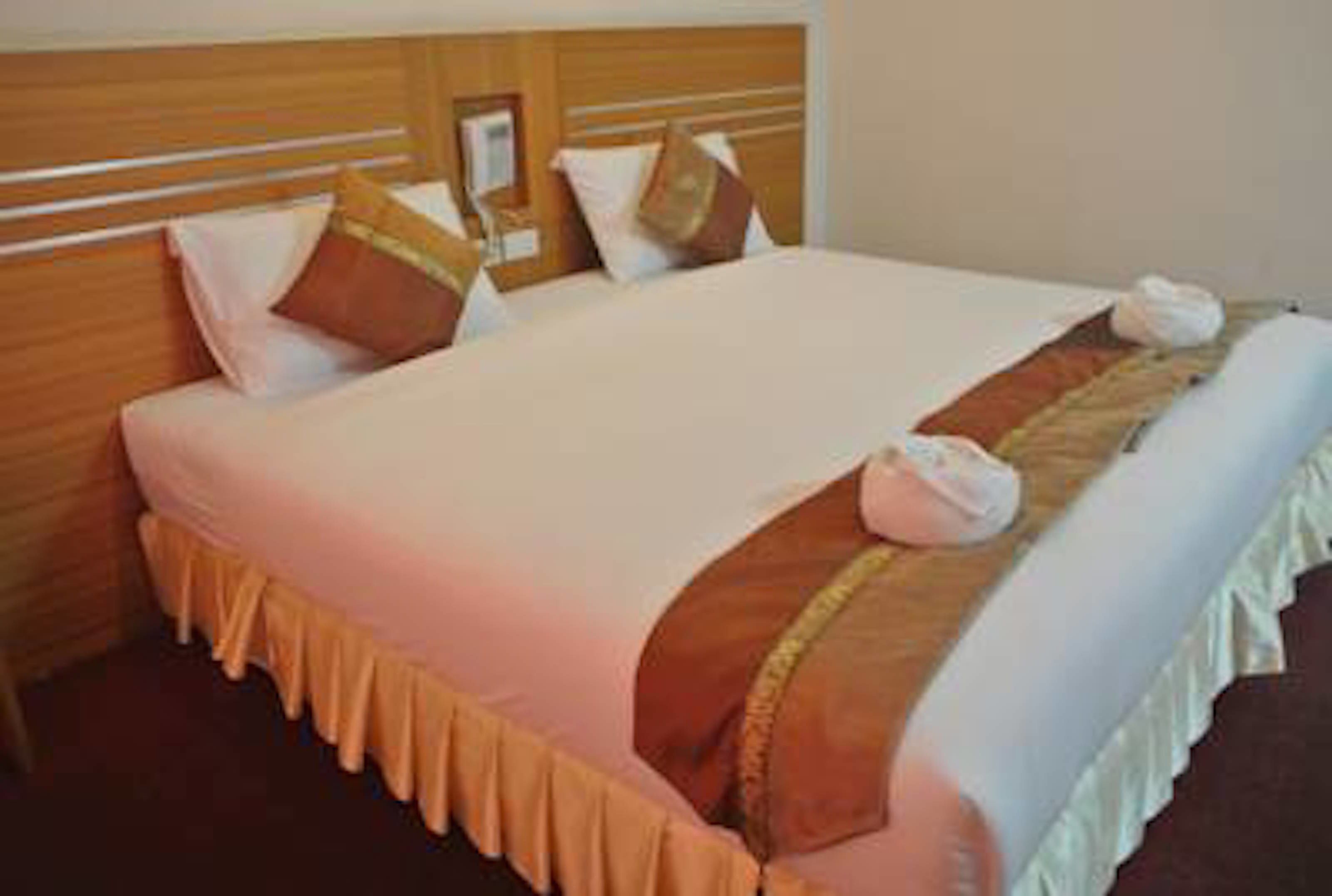 A hotel room with a neatly made bed, a wooden headboard, and a bedside table with a lamp.