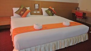 A hotel room with a large bed, a wooden headboard, a desk with a chair, and a red chair. - Chaikanathani Hotel (Phatthalung)